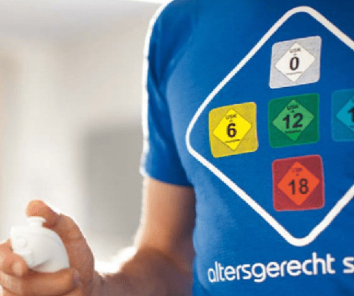 Ein Mann, der auf der Wii spielt und ein blaues T-Shirt mit USK-Sigeln trägt.