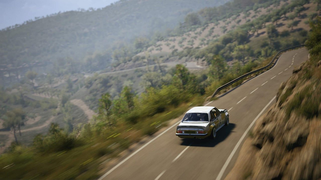Ein klassisches Rallyeauto fährt eine Bergschikane entlang.