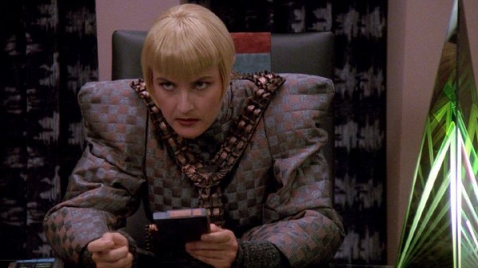 Durch den Topfschnitt und die blonden Haare verschwindet Selas Kopf im Hintergrund, sodass sie ihre ausdrucksstarken Augen und die rechteckige Uniform in Kombination wie eine missmutige Wohnzimmercouch wirken lassen.